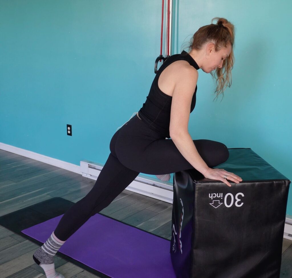 Dr. Chloe with her right knee on the box, standing leg walked out slightly behind her so she can stretch her glutes in the pigeon stretch